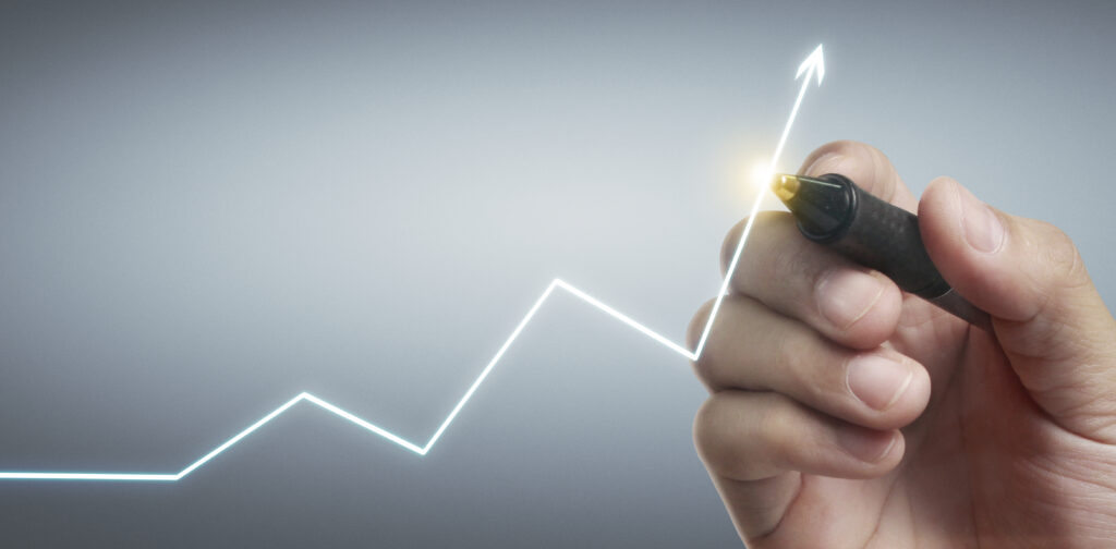 Mão segurando uma caneta aponta para um gráfico desenhado com linha ascendente, simbolizando crescimento financeiro e estratégias para maximizar o lucro.